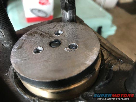 Close-up of a metal disc with three bolt holes and a central pin, attached to a larger assembly