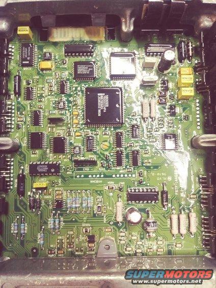 Close-up of a green circuit board with many black chips and yellow components. Text visible on one chip reads '9610-B'