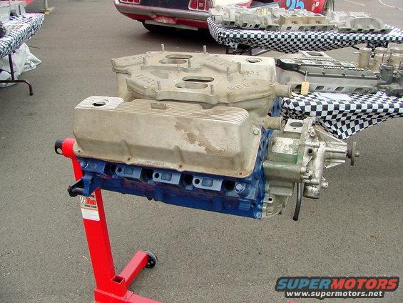 Ford V8 engine on red stand, with intake manifold and valve covers visible. Other engine parts on checkered tablecloths in background