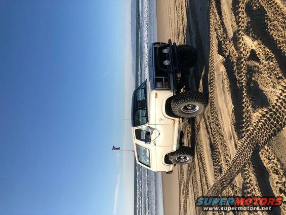 White 1981 Ford Bronco on beach with aftermarket bumper and off-road tires