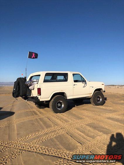 White Ford Bronco with spare tire on rear bumper parked on sand dunes