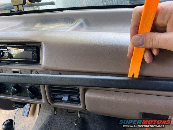 Dashboard of a 1996 Ford Bronco with an orange trim removal tool being used near the air vents