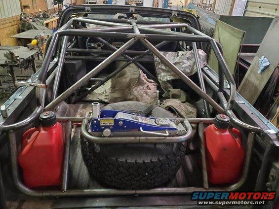 Roll cage installed in the bed of a 1978 Ford Bronco, with a spare tire, jack, and two red gas cans