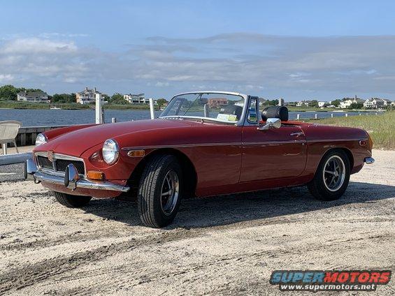 Red convertible with a white top parked on a sandy surface near water