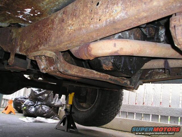 Undercarriage of a rusted truck, showing frame and exhaust system