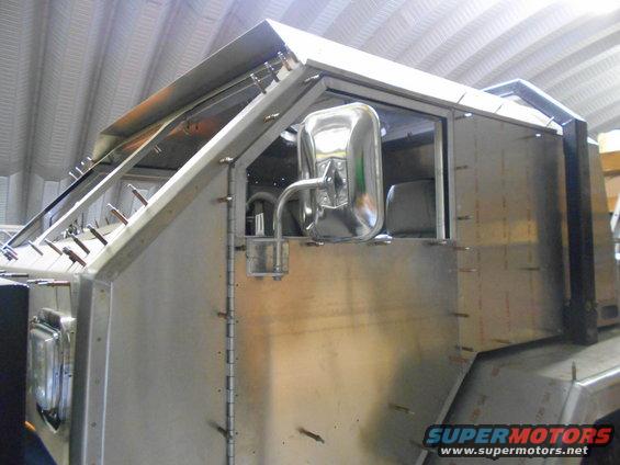 Unfinished metal vehicle body with chrome side mirror and visible interior seats