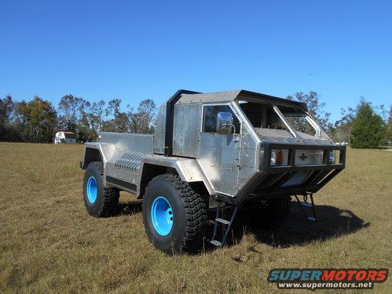 Custom off-road truck with aluminum body and bright blue wheels, parked in a grassy field