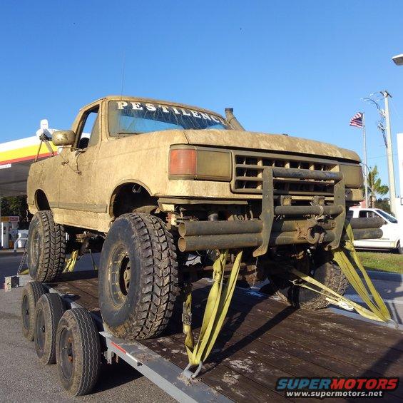 Mud-covered 1987 Ford F-250 pickup truck with large tires and a brush guard, secured to a trailer