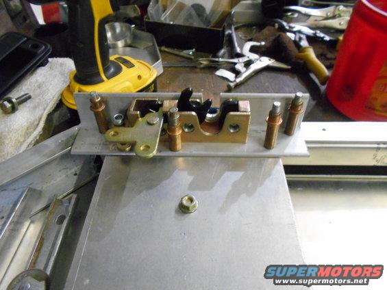 Door latch mechanism with brass and black metal components on a metal plate