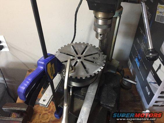 drill press holding a pulley with a clamp, drilling into it