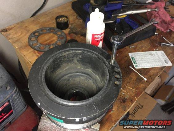 Crankshaft pulley with a socket wrench attached, on a wooden workbench with tools and a bottle of fluid