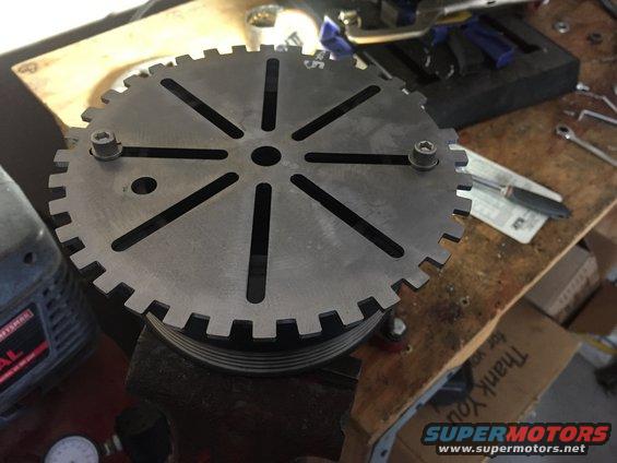 Metal pulley with gear teeth and slots, held in a vise