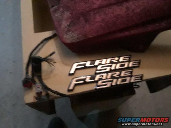 Two chrome 'Flare Side' emblems on a wooden surface