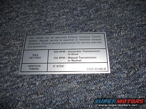 Emissions control sticker with idle setting and ignition timing information on a carpeted surface