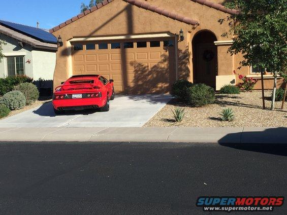 Red sports car parked in front of a house driveway. License plate is visible