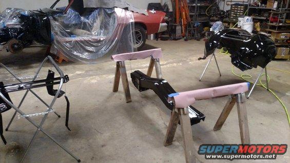 Black car parts on sawhorses in a garage with a red car body in the background