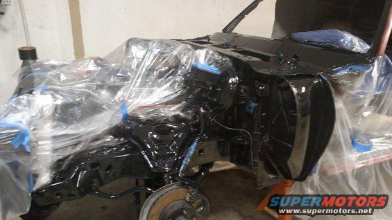 Car chassis covered in plastic sheeting, being prepped for paint. Some parts are black, others are still bare metal
