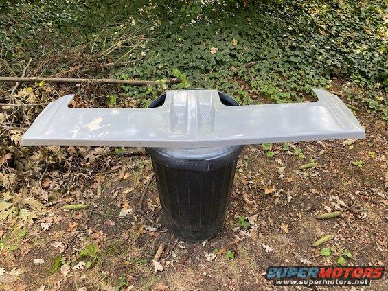 Gray rear spoiler resting on a trash can outdoors