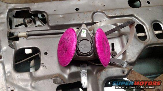 3M respirator mask with pink filters attached to the inside of a car door frame