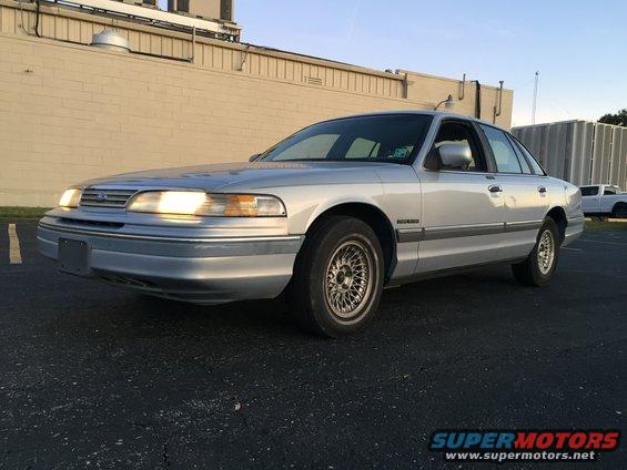 Silver 1994 Ford Crown Victoria parked outside a building. It has a mesh-style wheel