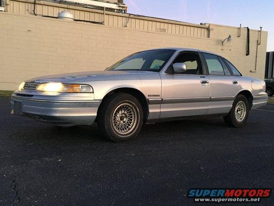 Silver sedan parked on asphalt, front 3/4 view. Headlights are on