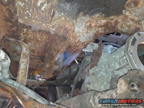 Heavily rusted vehicle undercarriage with visible suspension components and transmission housing