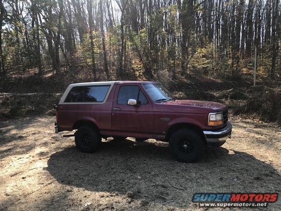 Maroon Ford Bronco parked on dirt road with trees in background