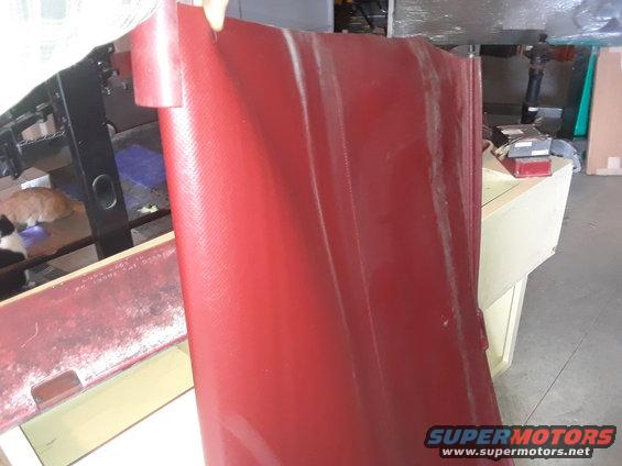red textured panel held up, with a workbench and cats in background