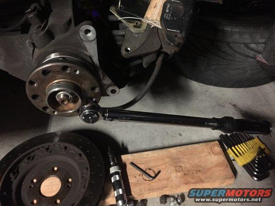 Car wheel hub assembly with a torque wrench attached, brake rotor, Allen wrenches, and a screwdriver on the ground