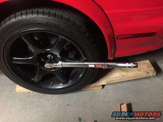 Using a torque wrench on a car's wheel, which is resting on wooden blocks