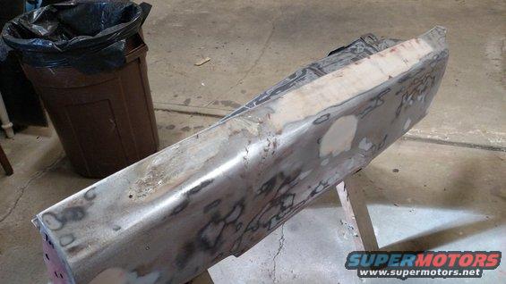 Metal car bumper with body filler and primer, resting on sawhorses