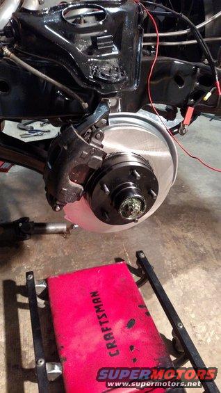 close-up of a car's front brake rotor and caliper assembly, with a red creeper in the foreground