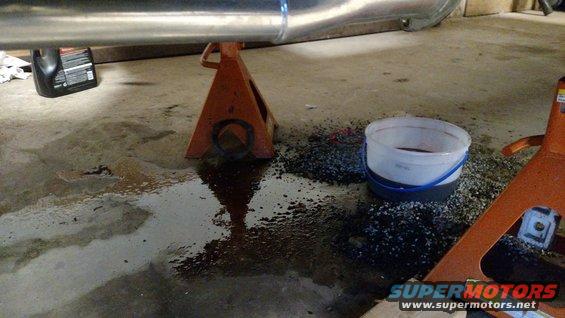 Underbody of vehicle on jack stands with spilled fluid and oil bottle