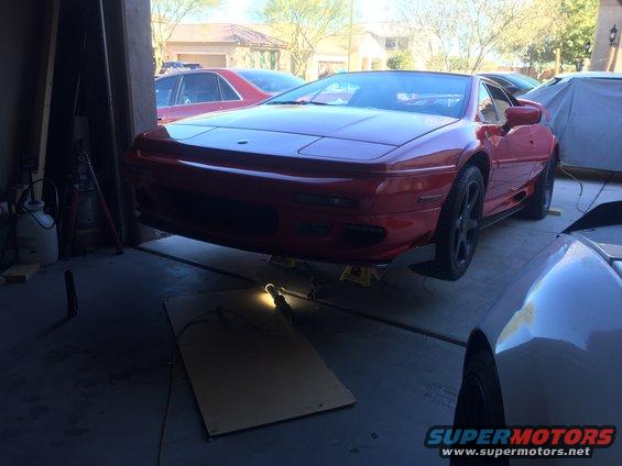 red sports car on jack stands in a garage, another car partially visible in foreground