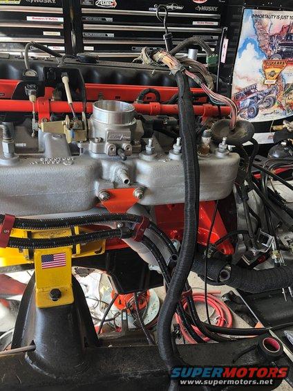 Engine assembly on a yellow stand, with a complex wiring harness and throttle body visible