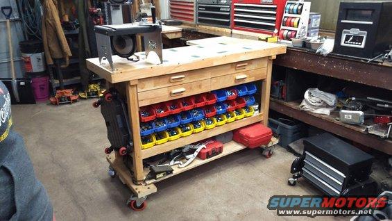 Workbench with red, blue, and yellow bins holding parts. A grinder is on top. Tools and storage units are around it