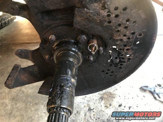 Wheel hub assembly with damaged rotor and caliper bracket. Greasy splined shaft visible