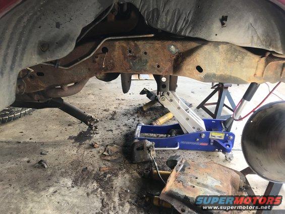 rusted frame, suspension, and jack stands under a vehicle