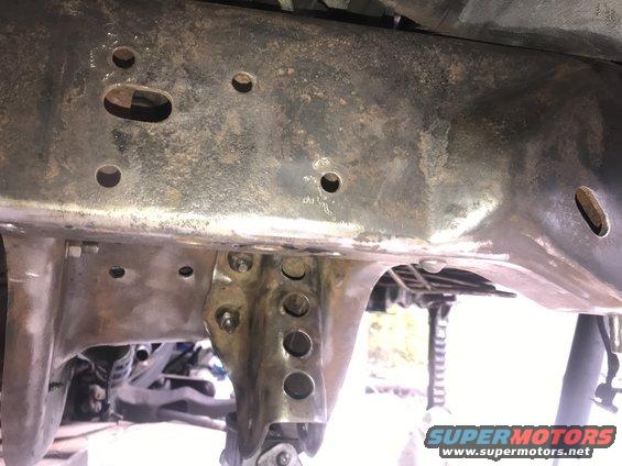 Rusty vehicle frame with holes and bolts, undercarriage view