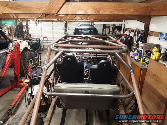 Interior view of a custom tube chassis buggy with two seats, a roll cage, and a dark SUV visible in the background
