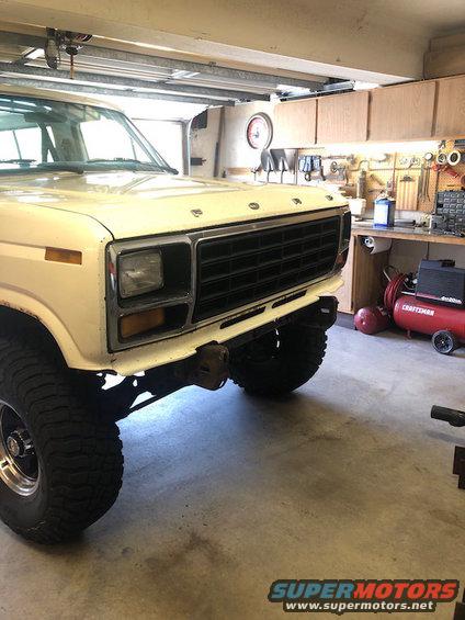 Front view of a cream-colored Ford Bronco in a garage. It has a black grille and large tires