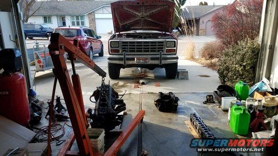 Red Ford truck with hood open, engine removed, parked in driveway
