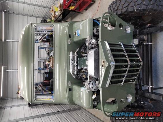 olive green truck body with engine exposed, large tires, in a garage