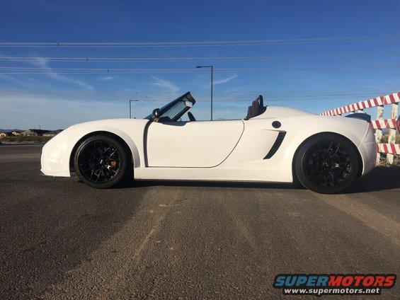 White convertible sports car with black wheels parked on asphalt, blue sky with power lines