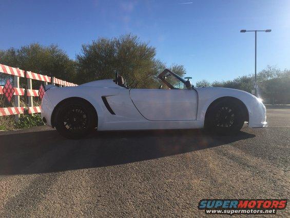 White convertible sports car parked next to a red and white striped fence