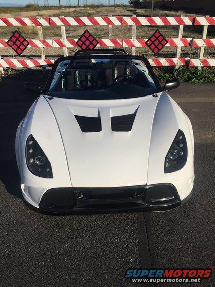 White convertible sports car with black racing seats, front view. Hood has dual vents. Black grille and headlights