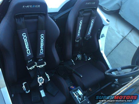 Car interior with two black Corbeau racing seats and NRG harnesses, a racing steering wheel, and a shifter