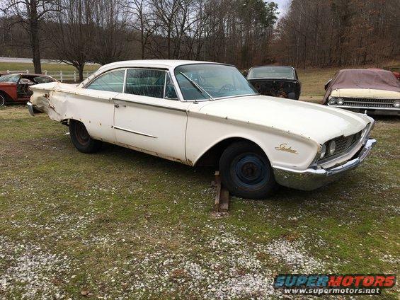1960 Ford Starliner coupe, white, with dented rear quarter panel. Other cars visible in background