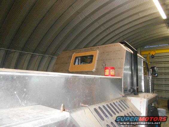 Custom truck build in garage with metal body panels and a small window. Red cans on shelf