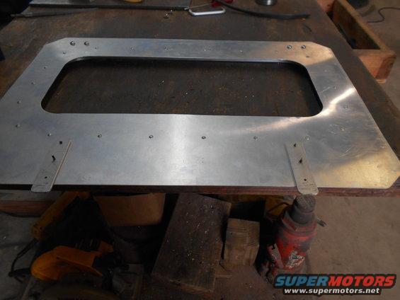 aluminum panel with a large rectangular cutout, resting on a workbench with tools and a jack visible